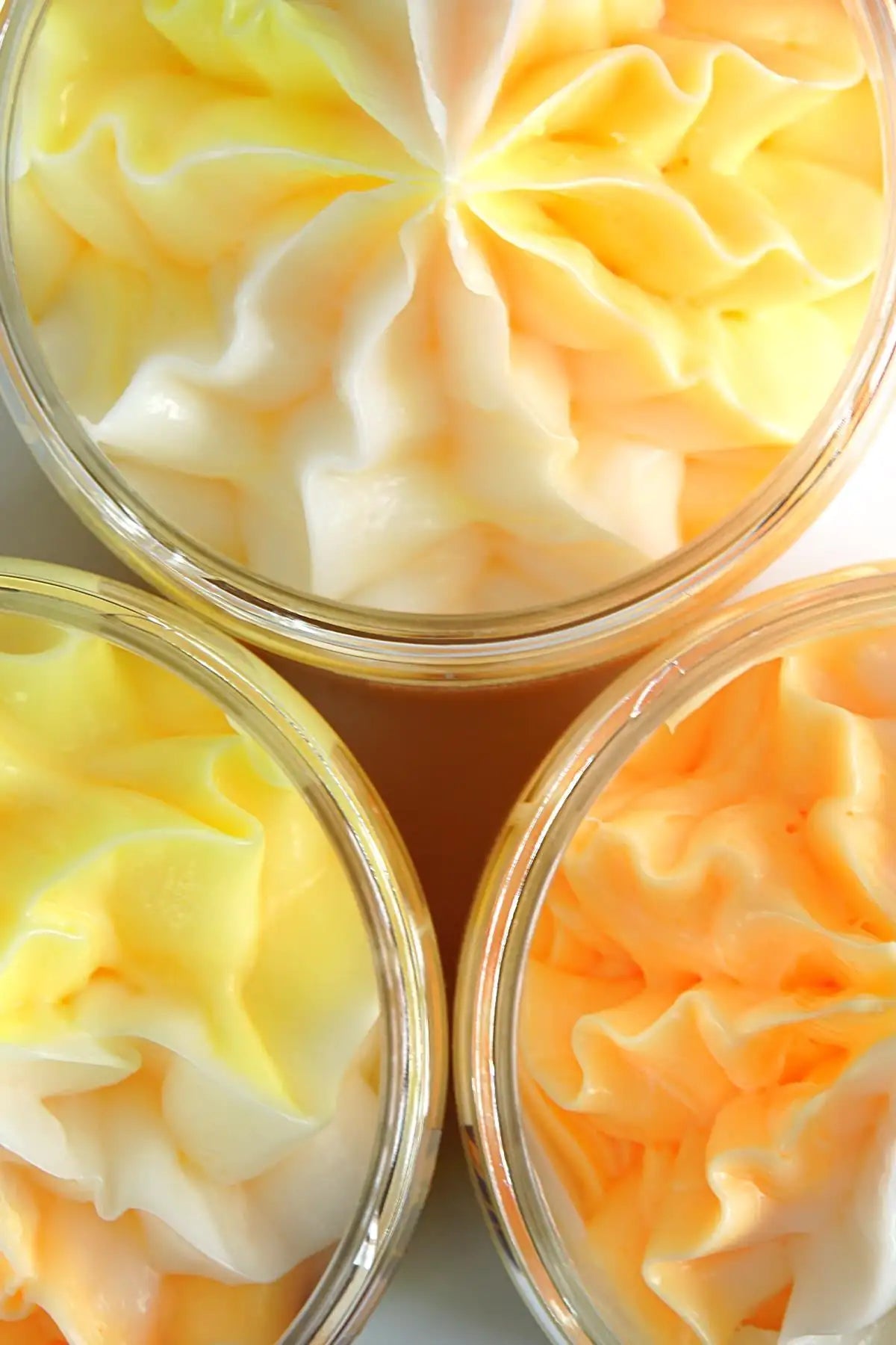 Three containers of yellow and white swirled soap on a light background
