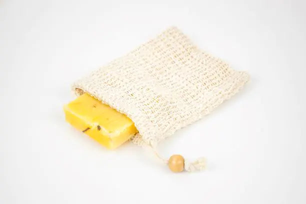 Yellow soap bar in a beige woven bag on a white background