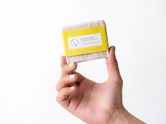 Hand holding a bar of soap with a yellow label against a white background