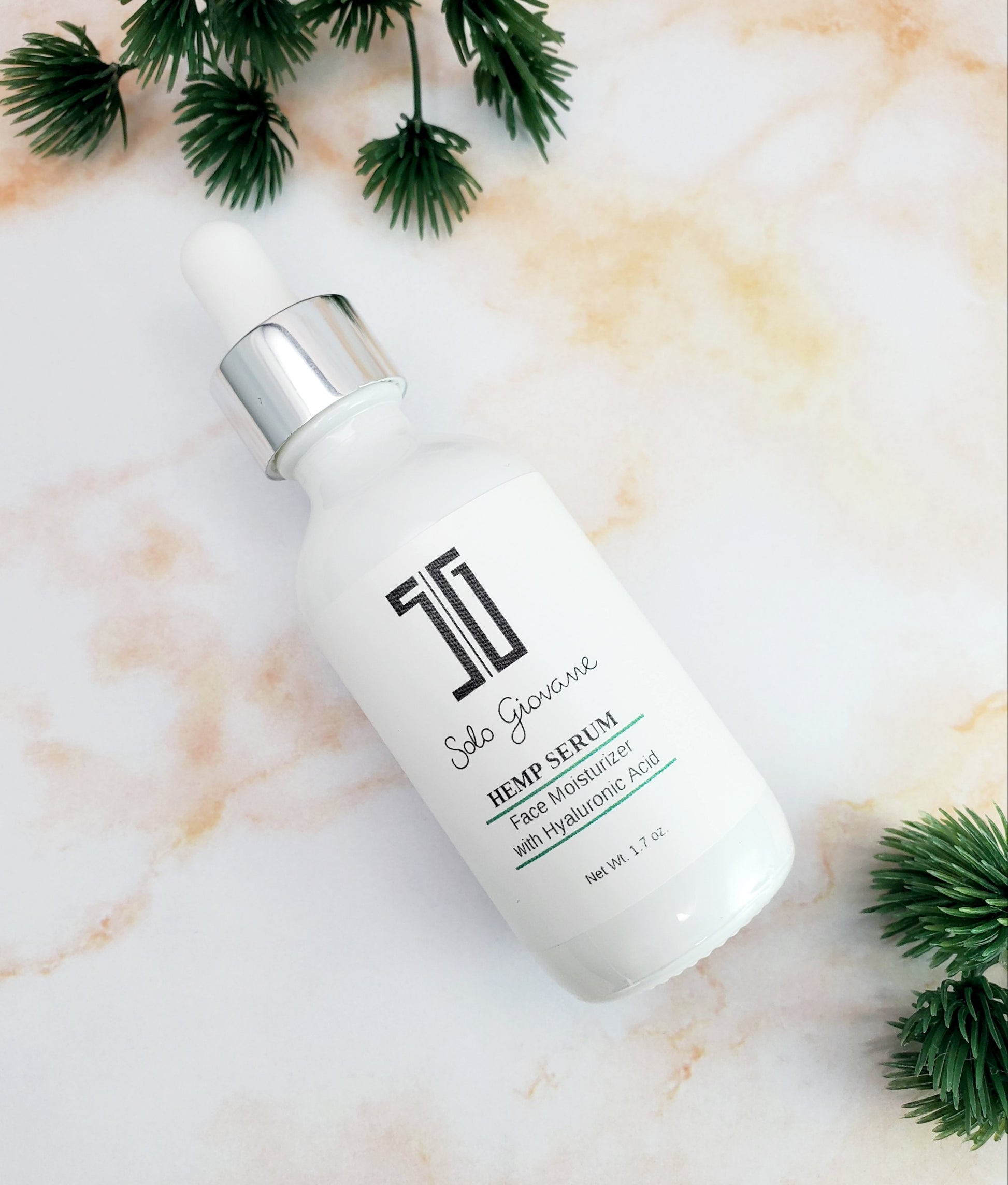 White serum bottle with silver cap on a marble surface with green leaves