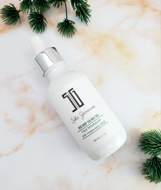 White serum bottle with silver cap on a marble surface with green leaves