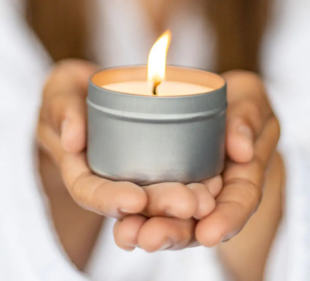 Hands holding a small lit candle in a tin container against a blurred background